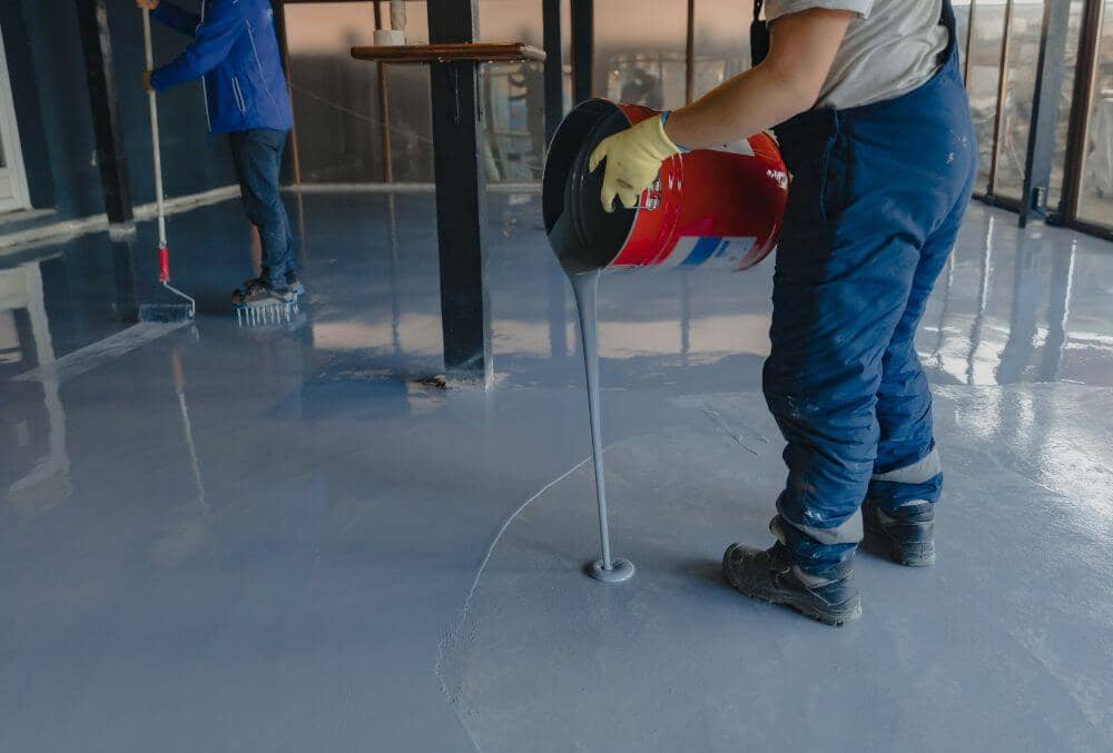 Two workers spreading gray epoxy in a commercial building