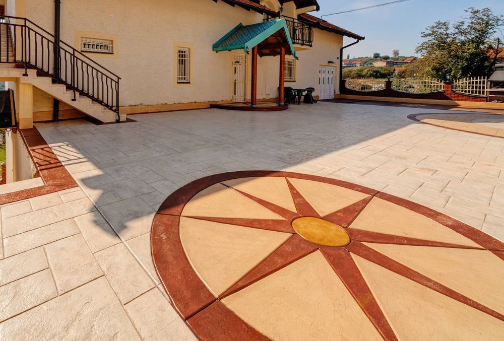 Stamped concrete driveway featuring an engraved sun pattern with decorative coloring and sealed finish